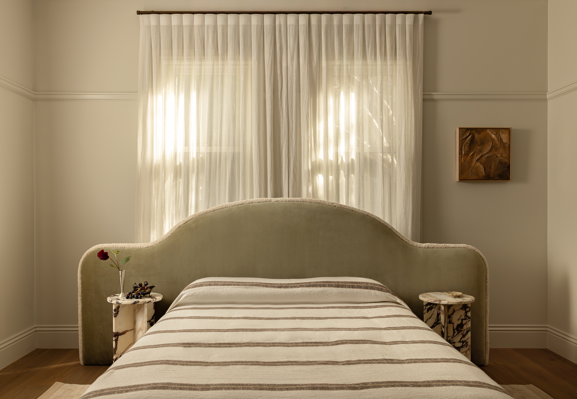 A neatly made bed featuring the Paloma striped blanket, paired with a velvet headboard, two compact bedside tables, and sheer curtains draping over a sunlit window.